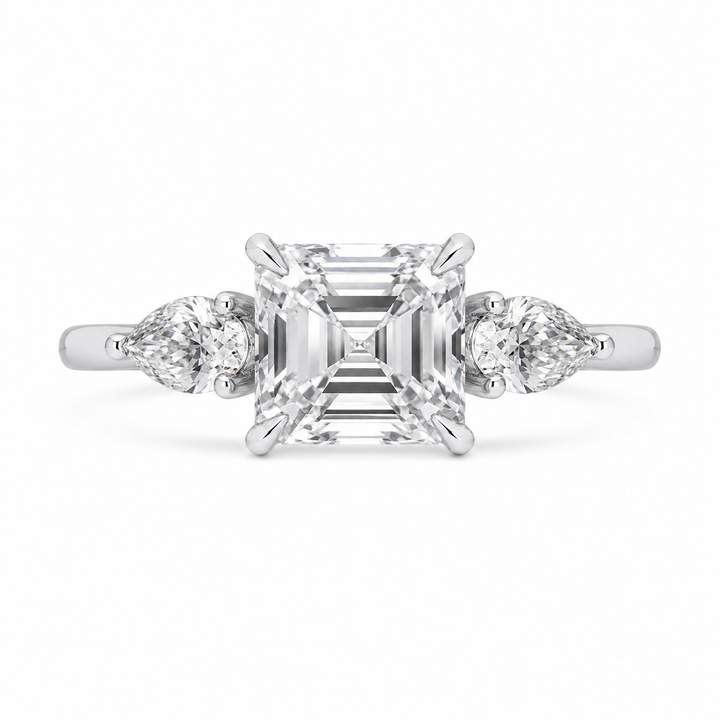 Diamond ring with a central asscher-cut diamond flanked by two pear-shaped diamonds on a white background